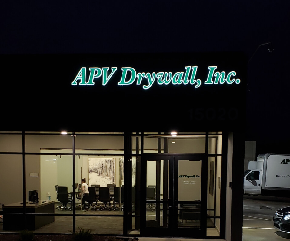 APV drywall in green channel letters on storefront lit at night with white reveal
